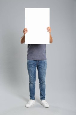 Gri arka planda beyaz boş poster tutan adam. Tasarım için model