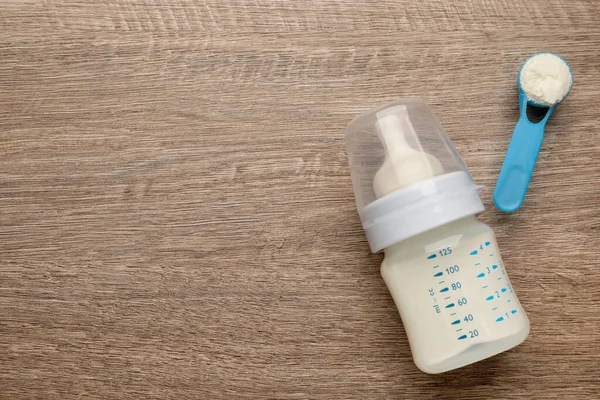 Feeding bottle with infant formula and powder on wooden table, flat lay. Space for text