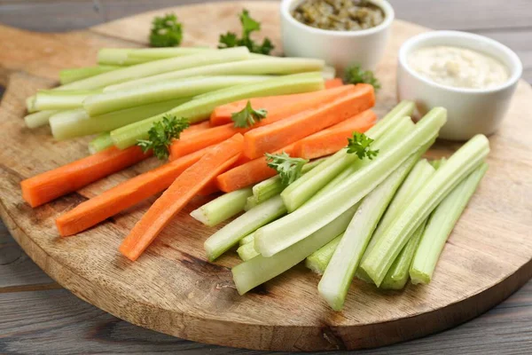 Celery and other vegetable sticks with different sauces on wooden board