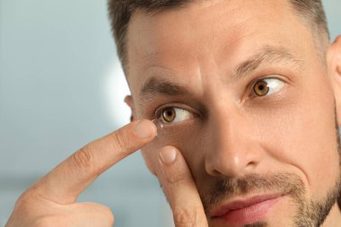 Man putting contact lens in his eye on blurred background, closeup