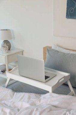 White tray table with laptop on bed indoors