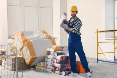 Professional builder in uniform with bag of cement indoors