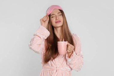 Beautiful young woman in bathrobe with cup of coffee on light background