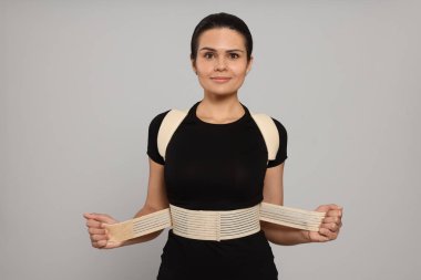 Beautiful woman with orthopedic corset on grey background