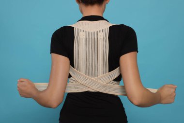 Closeup of woman with orthopedic corset on blue background, back view