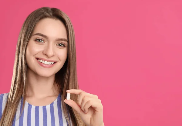 Young woman with vitamin pill on pink background. Space for text