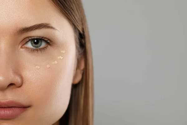 Young woman with cream around eye on light grey background, closeup. Space for text