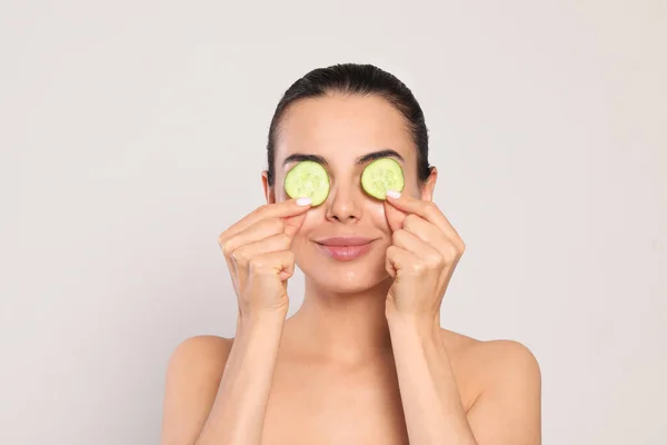 Beautiful Young Woman Putting Slices Cucumber Eyes Light Grey Background — Stockfoto