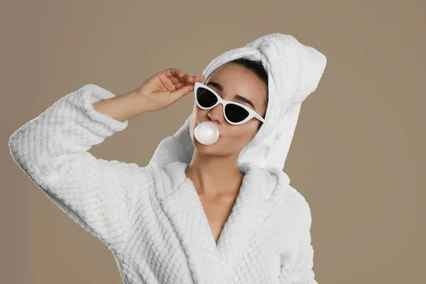身穿浴衣 戴着太阳镜 在褐色背景下吹口香糖的年轻女子 — 图库照片