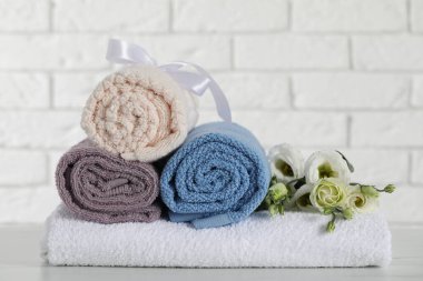Rolled and folded towels with flowers on white table, closeup