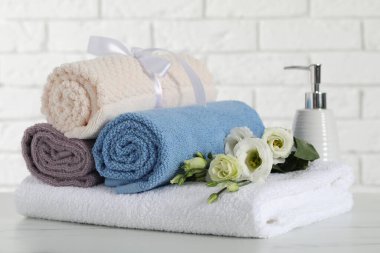 Rolled and folded towels with flowers on white table, closeup