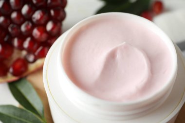 Jar with natural facial mask, pomegranate seeds and green leaves, closeup