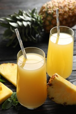 Delicious pineapple juice and fresh fruit on black wooden table, closeup
