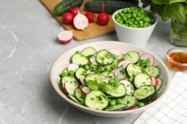 Appetizing salad with cucumbers, radish and pea in bowl on light grey table
