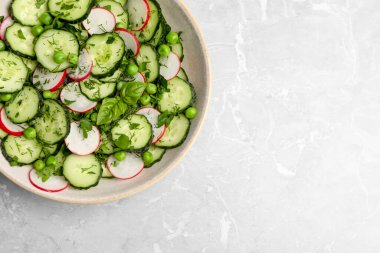Appetizing salad with cucumbers, radish and pea in bowl on light grey table, top view. Space for text