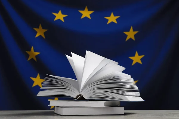 Books on light grey table against flag of European Union