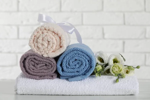 Rolled and folded towels with flowers on white table, closeup