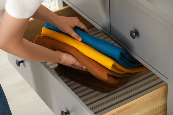 Woman putting clean clothes into drawer at home, closeup