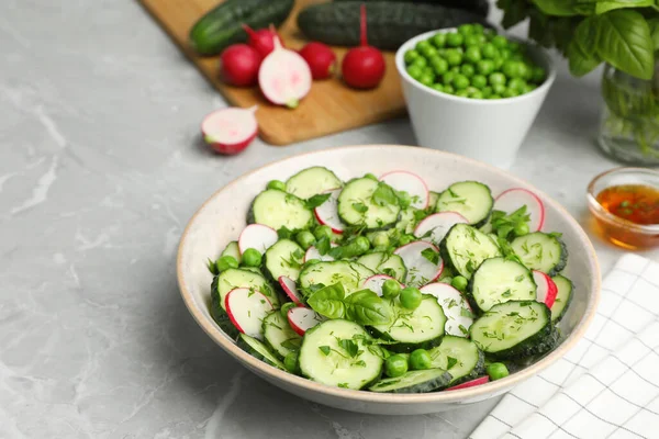 Appetizing salad with cucumbers, radish and pea in bowl on light grey table