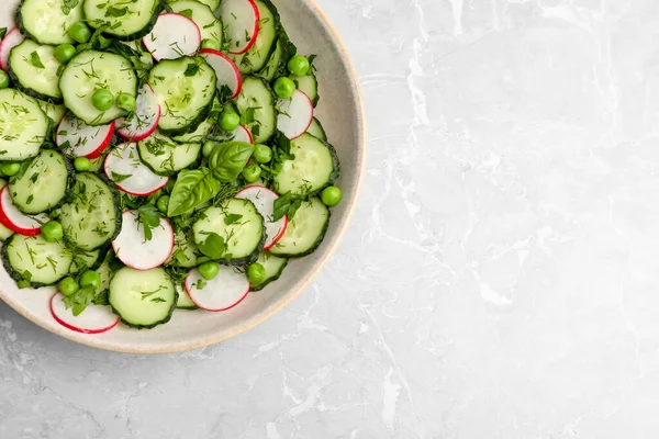 Appetizing salad with cucumbers, radish and pea in bowl on light grey table, top view. Space for text