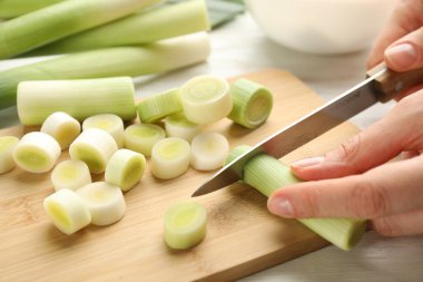 Woman cutting fresh raw leek on wooden board at table, closeup
