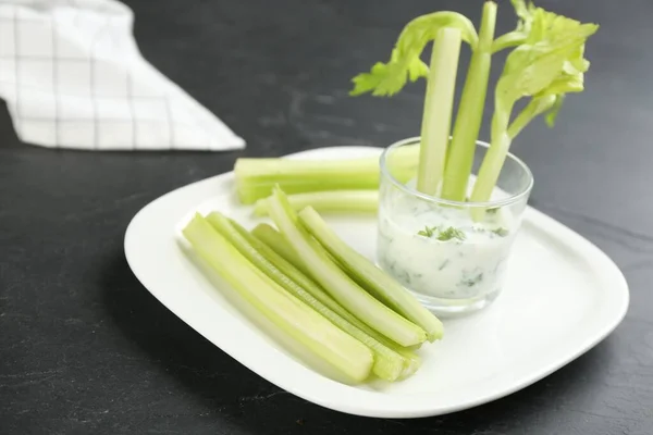 Celery sticks with dip sauce in glass on black table, closeup