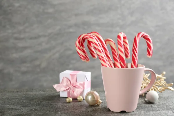 Candy canes in cup and Christmas decor on grey table, space for text