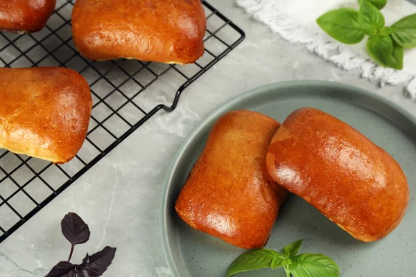 Delicious baked pirozhki and basil on light grey marble table, above view