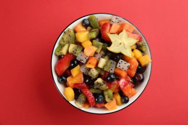 Delicious exotic fruit salad on red background, top view