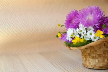 Bouquet of beautiful wildflowers in wicker basket on wooden table. Space for text