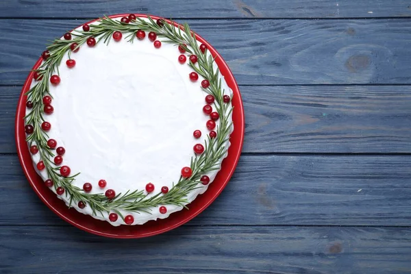 Traditional Christmas cake decorated with rosemary and cranberries on blue wooden table, top view. Space for text