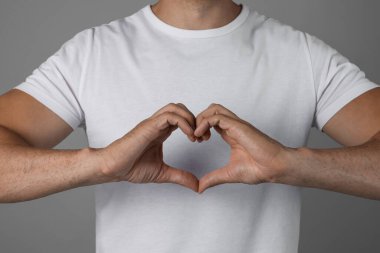 Man making heart with hands on grey background, closeup