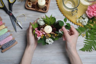 Woman making floral composition with candle at wooden table, top view. Master class