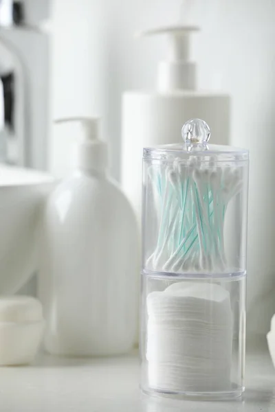 Containers with cotton swabs and pads near cosmetic products on white countertop in bathroom