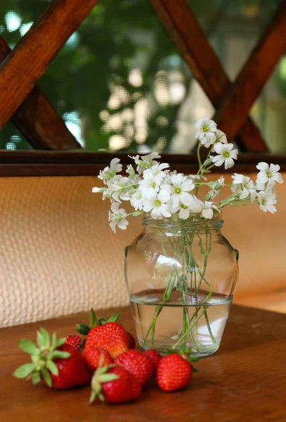 Fresh strawberries and bouquet of beautiful white flowers on wooden table