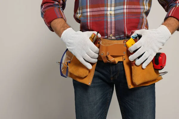 Professional builder with tool belt on light background, closeup