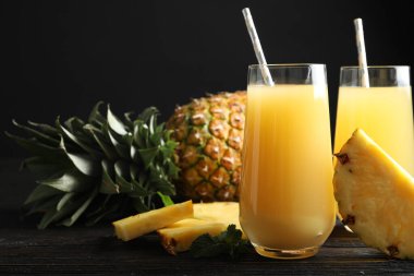 Delicious pineapple juice and fresh fruit on black wooden table, closeup