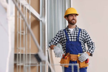 Professional builder in uniform with tool belt indoors