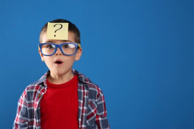 Emotional little boy with question mark on blue background, space for text