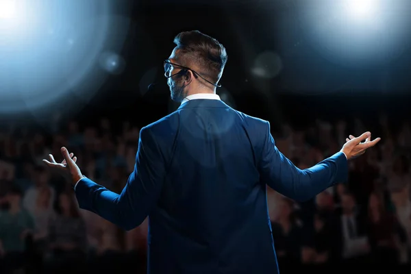 Motivational speaker with headset performing on stage, back view