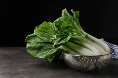 Fresh green pak choy cabbages with water drops in sieve on grey table