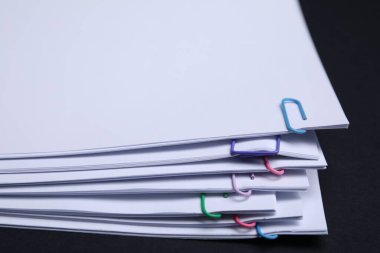 Sheets of paper with clips on black background, closeup