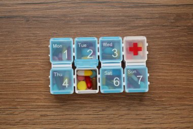 Plastic box with different pills on wooden table, top view
