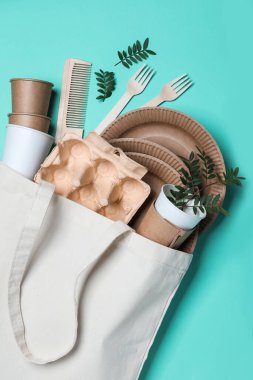 Eco bag with different disposable items on turquoise background, flat lay. Recycling concept