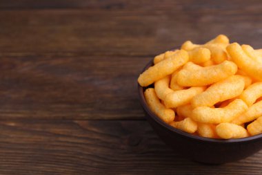 Bowl with crunchy cheesy corn snack on wooden table, closeup. Space for text