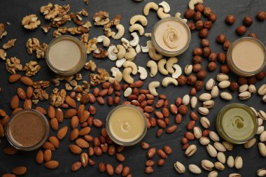 Farklı türde lezzetli fındık ezmesi ve malzemeler siyah masada, düz yerde.