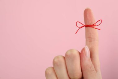 Pembe arkaplanda hatırlatma olarak bağlı kırmızı yay ile işaret parmağı gösteren kadın, yakın plan, metin için boşluk