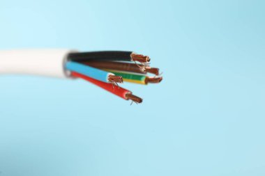 Cable with stripped electrical wires on light blue background, closeup
