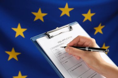 Woman filling visa application form against flag of European Union, closeup