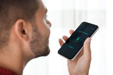 Genç adam akıllı telefondan kapalı alanda ses araması yapıyor.